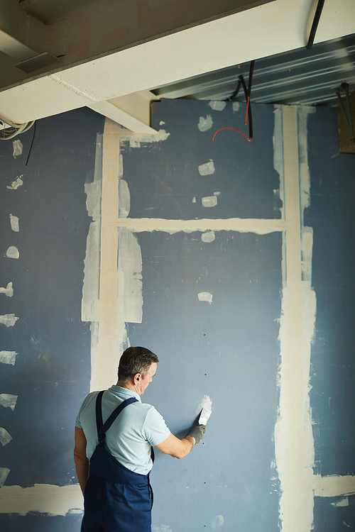 Vertical back view portrait of senior man working on dry wall while renovating house, copy space