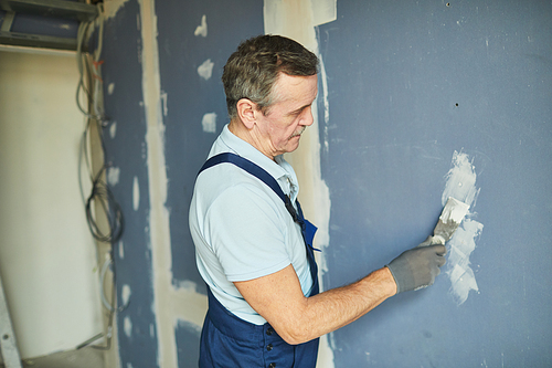 Side view portrait of senior man working on dry wall while renovating house, copy space