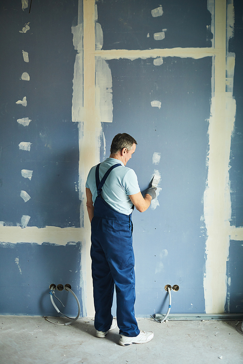 Full length back view portrait of senior man working on dry wall while renovating house, copy space