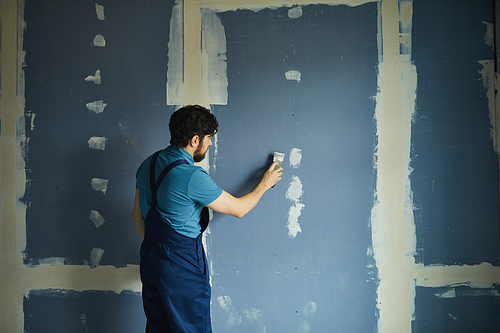 Back view portrait of bearded man working on dry wall while renovating house, copy space