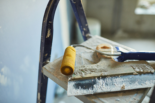 Background image of used spatula and paint roller lying on top of ladder on construction site or in house building, copy space