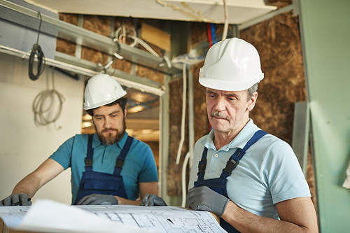 Portrait of senior construction worker wearing hardhat while looking at floor plans while renovating house, copy space