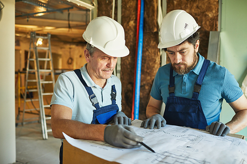 Waist up portrait of two construction workers wearing hardhats while looking at floor plans while renovating house, copy space