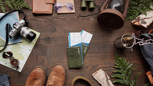 Above view of foreign passports and plane tickets on wooden table with twigs, boots, thermos mug and camera, flat lay