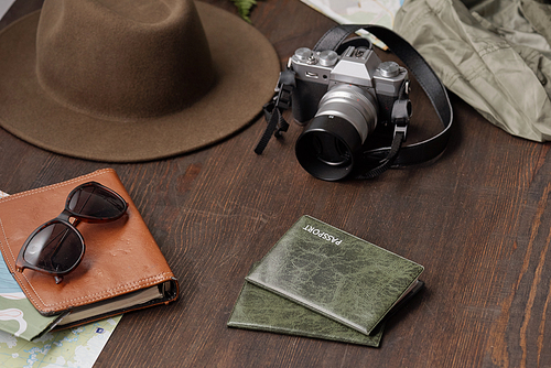 Close-up of tourists stuff such as passports in covers, photographic camera, hat and eyeglasses on dark wooden table