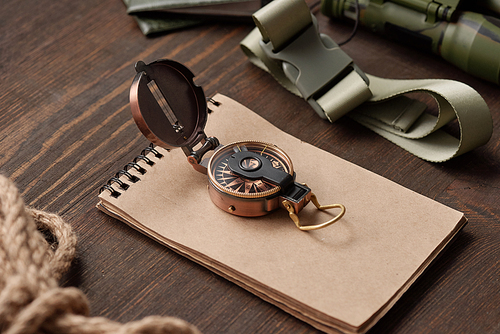 Close-up of open compass on sketchpad, belt and rope on dark wooden table, hiker stuff concept