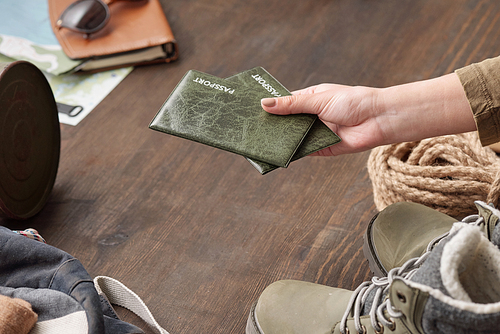 Close-up of unrecognizable woman packing passports when going to travel, hand above wooden table with hiking stuff