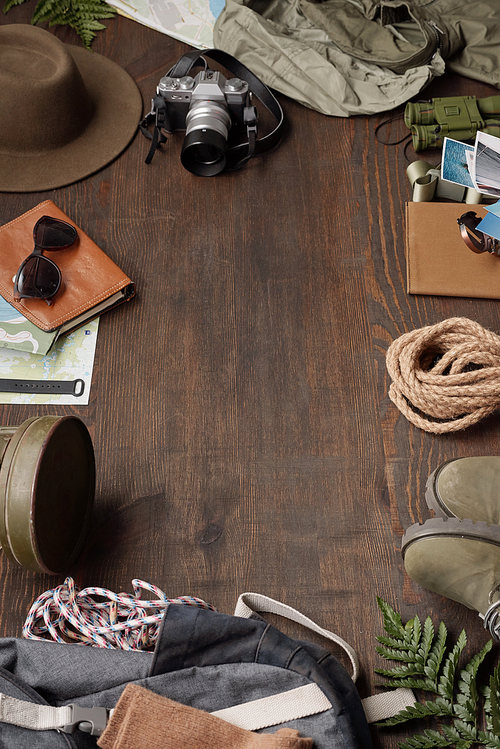 Tourism flat lay: camera, hat, rope, maps, boots, binoculars and backpack in circle, copy space