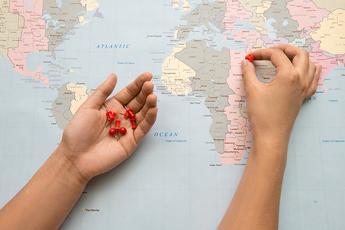 Close-up of unrecognizable tourist putting red pins on paper map while making place to visit