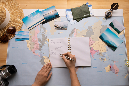 Above view of unrecognizable traveler composing check list in diary while planning trip