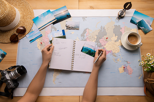 Above view of unrecognizable woman sitting at table with world map and making notes about sights