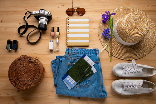 Above view of jeans, sun hat, flower, camera, bag, tickets, nail polishes and sneakers on table, travel knolling