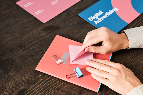 Hands of young office manager sitting by wooden table and taking pink notepaper while going to make short working reminder or plan points