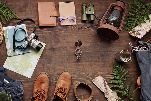 Above view of navigational compass among travelers stuff such as lantern, camera, thermos mug and boots on wooden table