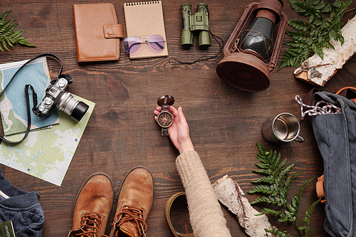 Above view of unrecognizable female hiker checking compass while packing stuff for new adventure in forest, flat lay