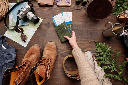 Above view of female hand preparing tickets with passports while packing stuff for hiking trip, flat lay