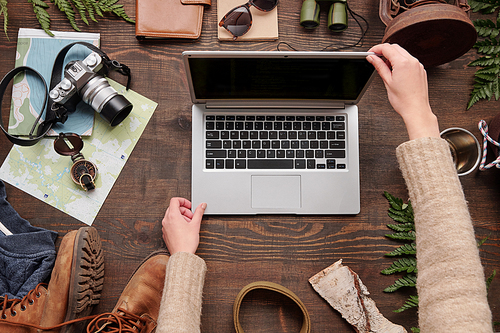 Above view of unrecognizable woman in sweater opening laptop while prepare to search for hiking location on internet, flat lay