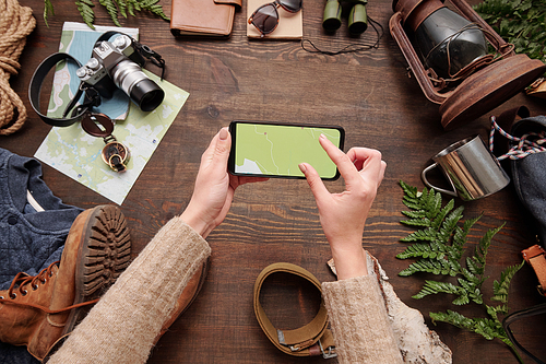 Above view of unrecognizable woman watching online map on smartphone while preparing for hiking, tourism flat lay