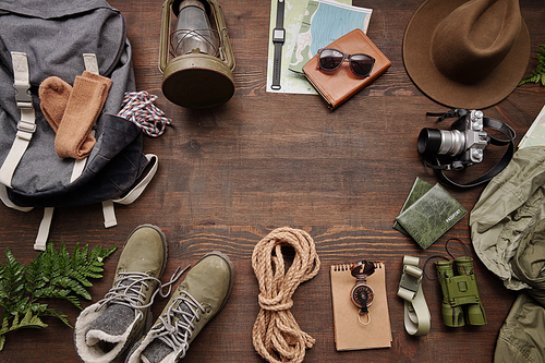 Above view of backpack, rope, boots, compass, binoculars, hat, lantern and maps on wooden table, hiking flat lay