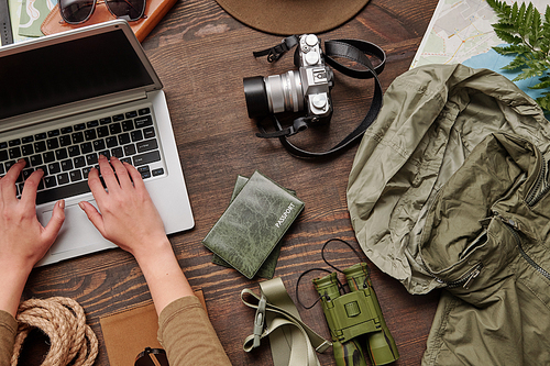 Above view of unrecognizable woman using laptop while buying airline tickets online and planning hiking trip, flat lay