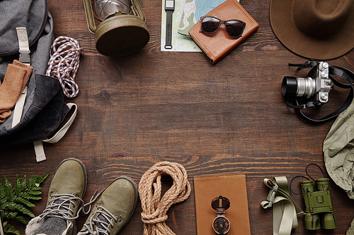 Hiking frame composition with rope, compass, photographic camera, backpack, boots on wooden table, flat lay