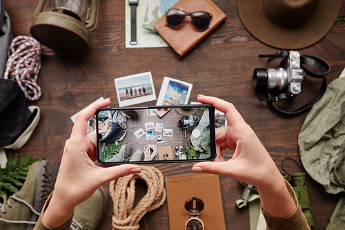 Above view of unrecognizable hiker using smartphone while photographing travel composition on table