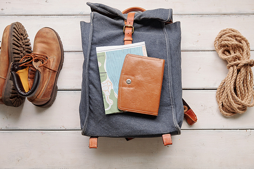 Above view of hiking backpack with map and purse placed on wooden floor with boots and rope, flat lay