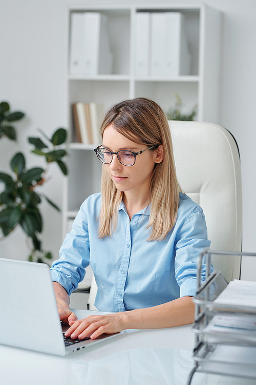 Serious young businesswoman or office secretary looking through data on laptop display, making working plan or preparing presentation