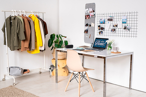 Workplace of contemporary fashion designer with jackets handing on rack along wall and desk with laptop and other supplies on desk