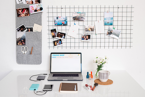 Workplace of contemporary female photographer or designer with laptop, notebook, smartphone, cosmetic products, mug and flowers