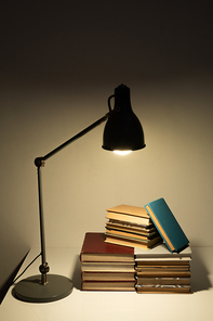 Light of lamp falling on pile of books or manuals of contemporary school or college student on desk in dark room at night