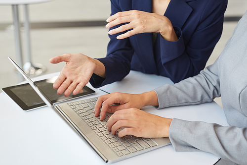 Cropped portrait of two successful businesswomen discussing work and gesturing and using laptop together, copy space