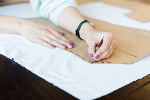 Close-up of unrecognizable woman using pins while attaching sewing pattern to fabric at table