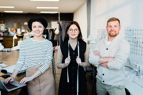 Portrait of smiling confident stylish colleagues standing in modern tailoring studio