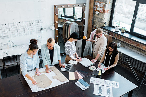 Two small groups of professional fashion designers working over new sketches and paper patterns by table in workshop