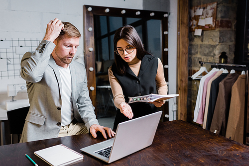 Distraught chef designer with sketchbook pointing at laptop monitor while blaming manager for mistake in order