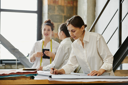 Two young female designers of clothes phoning clients about orders while their colleague measuring length of paper patterns near by