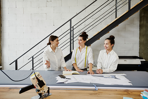 Group of three young fashion designers in white shirts brainstorming and discussing ideas for new seasonal collection at meeting