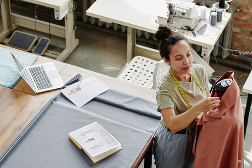 Young modern worker of fashion design studio sewing clothing item on dummy while working over new seasonal collection in workshop