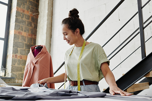 Young self-employed fashion designer or tailor looking at sketch of seasonal collection items and choosing suitable textile for them