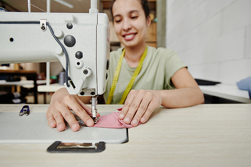 Hands of happy young tailor by electric sewing machine working over shoulder pads for new dress, coat or other clothing item