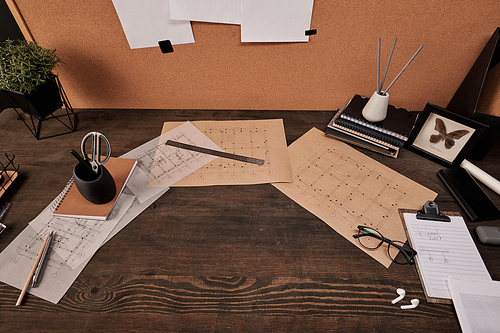 Carton board with papers, blueprints, ruler, eyeglasses, copybooks and other office supplies surrounding copyspace on wooden table