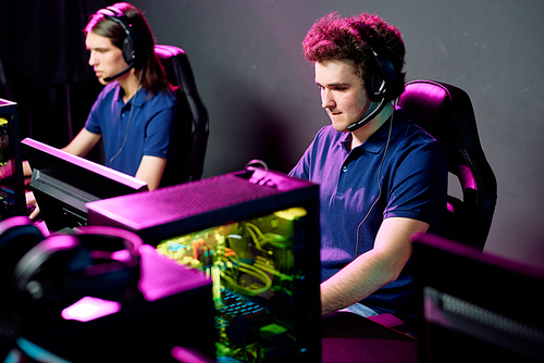 Row of concentrated young e-sport gamers in headsets with microphones sitting in front of computers