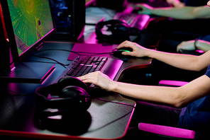 Close-up of unrecognizable cyber sport gamer sitting at table with headphones and playing online game
