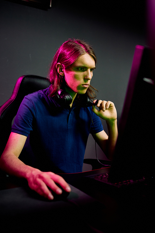 Serious young programmer focused on computer problem wearing headphones around neck working in dark office