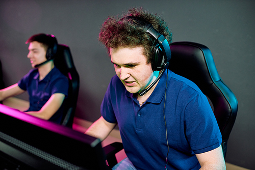Young operator of e-sport call center in headset looking at computer screen while commenting network game with tense expression