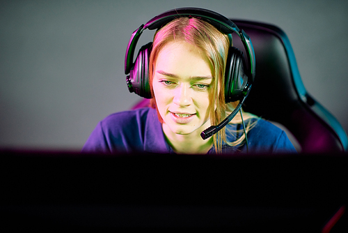Young female operator in headset looking at computer screen while consulting clients or gamer playing e-sport video game in club