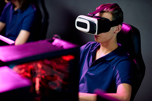 Serious young gamer in virtual reality headset playing videogame in modern cybersports club