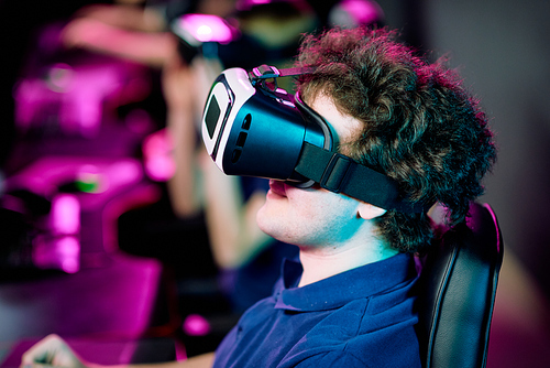 Side view of positive young curly-haired gamer playing videogame in virtual reality goggles