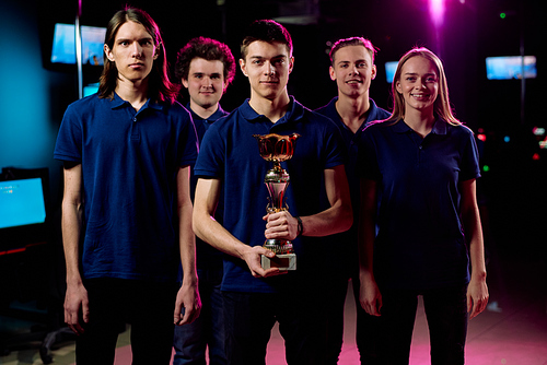 Team of five young champions in cybersports and network gaming competition standing in row in contemporary e-sports club